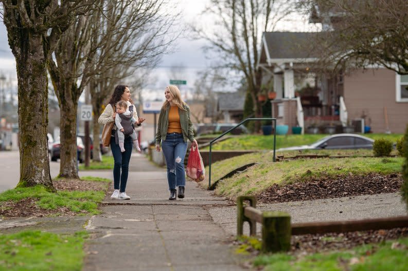 Two people with a child walking down a residential street carrying groceries.